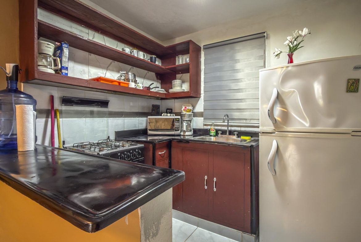 buyDRproperty Cozy kitchen with dark wood cabinets, white fridge, gas stove, microwave, and breakfast bar. Sosua Real Estate