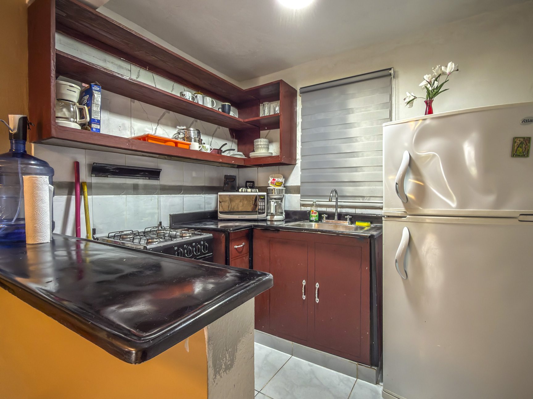 buyDRproperty Cozy kitchen with dark wood cabinets, white fridge, gas stove, microwave, and breakfast bar. Sosua Real Estate