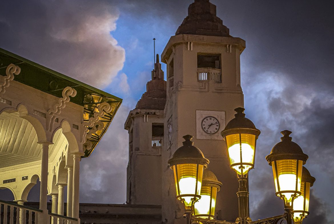 buyDRproperty Illuminated clock tower and gazebo at night under a dramatic, cloudy sky. Sosua Real Estate