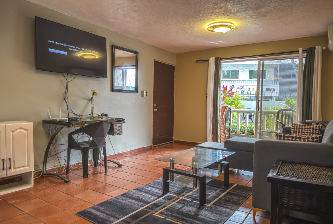 buyDRproperty Cozy living room with TV displaying a Netflix error message, glass coffee table, and outdoor view. Sosua Real Estate