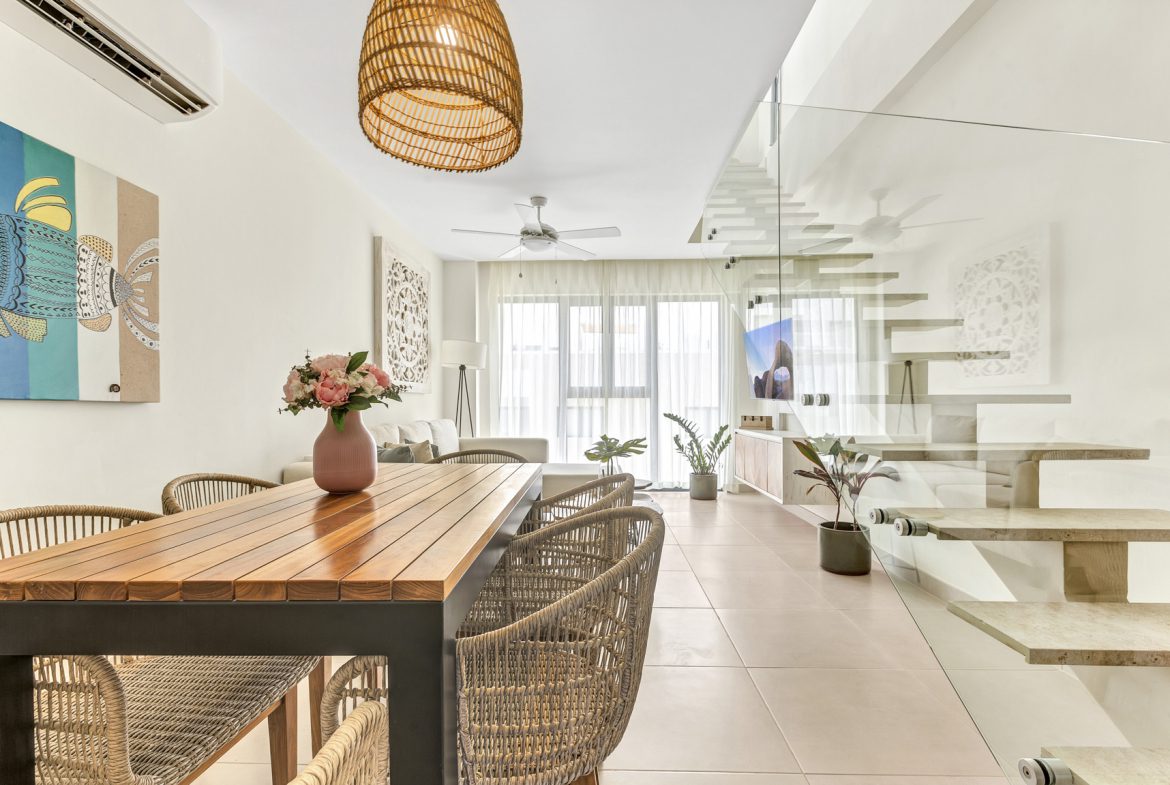 buyDRproperty Modern living room with dining area, featuring a wooden table, wicker chairs, and a unique staircase design. Sosua Real Estate