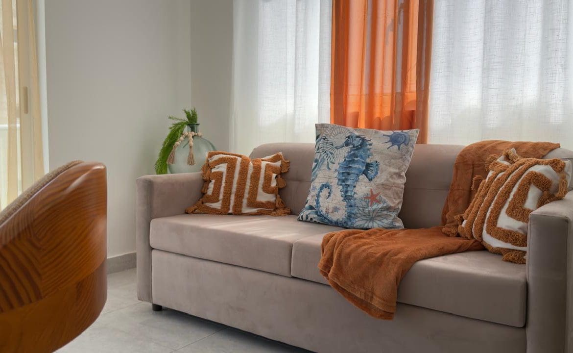 buyDRproperty Beige sofa with decorative pillows and a throw blanket in a bright, airy living room. Sosua Real Estate