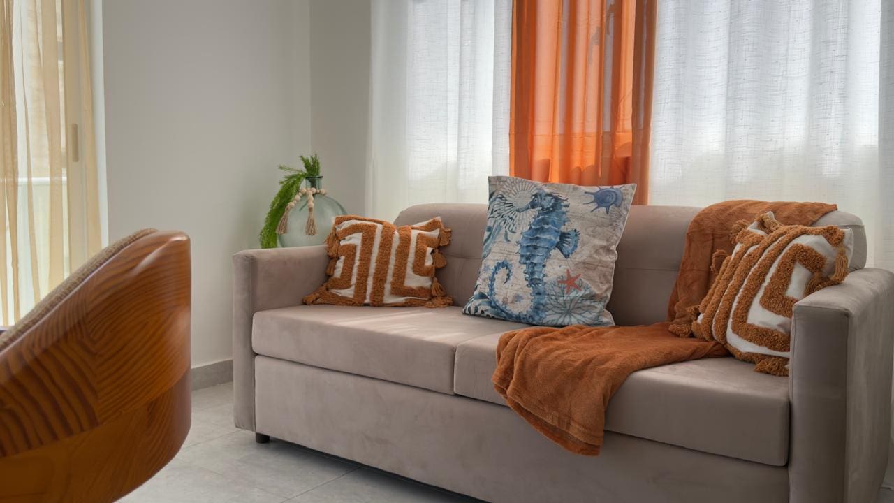 buyDRproperty Beige sofa with decorative pillows and a throw blanket in a bright, airy living room. Sosua Real Estate