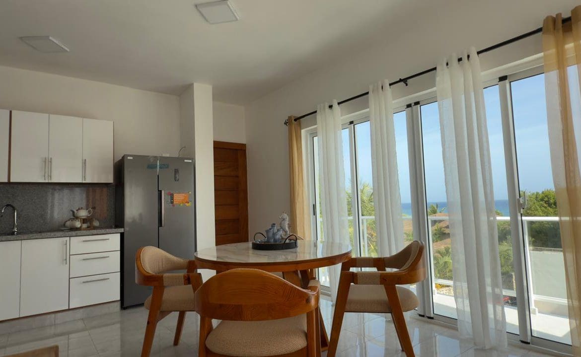 buyDRproperty Bright dining area with round table, chairs, and large windows with ocean view. Sosua Real Estate