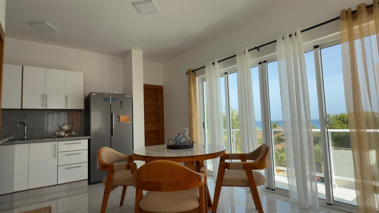 buyDRproperty Bright dining area with round table, chairs, and large windows with ocean view. Sosua Real Estate