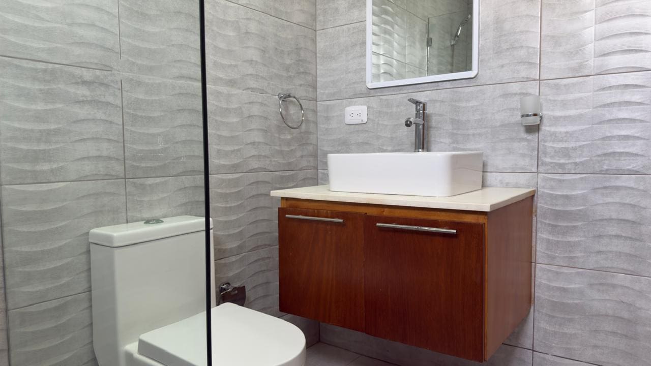 buyDRproperty Modern bathroom with gray wave tile, floating wood vanity, and white square sink. Sosua Real Estate