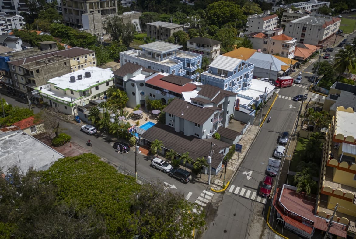 Aerial view of a tropical town street with colorful houses, palm trees, and parked cars.