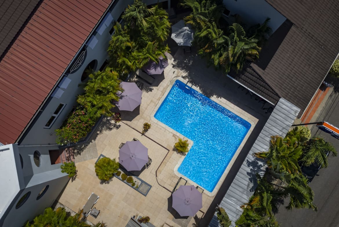buyDRproperty Aerial view of a resort pool with lounge chairs and umbrellas, surrounded by palm trees. Sosua Real Estate
