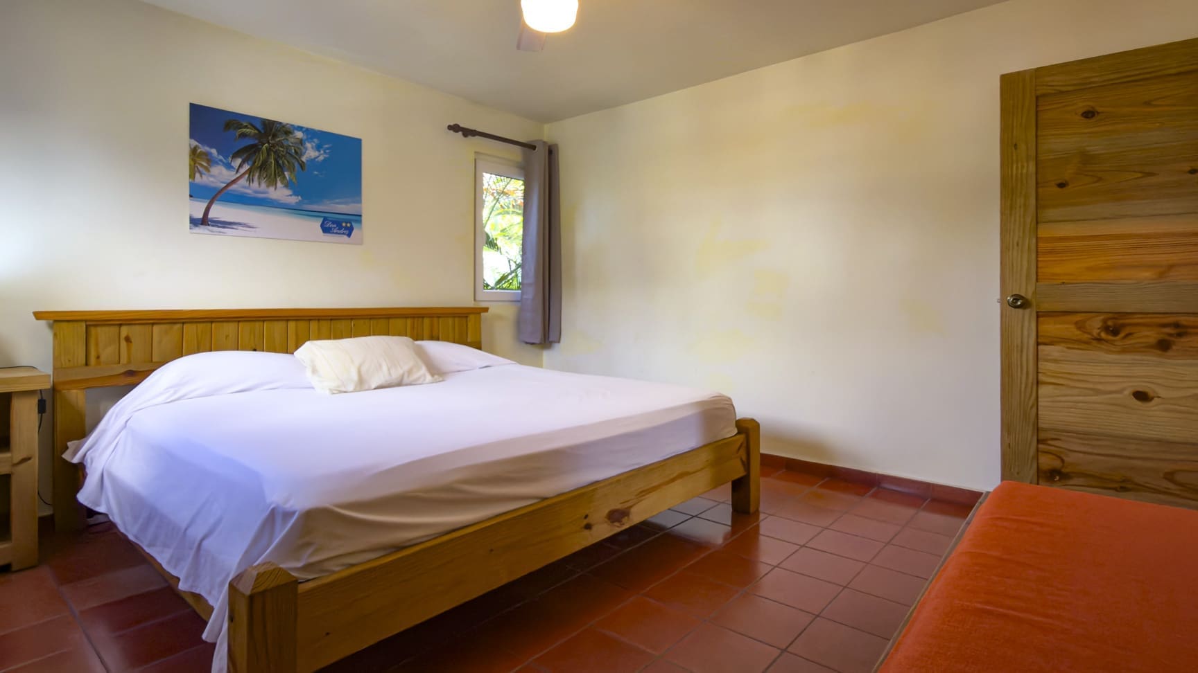 buyDRproperty Cozy bedroom with a wooden bed, white linens, and a tropical palm tree painting. Sosua Real Estate