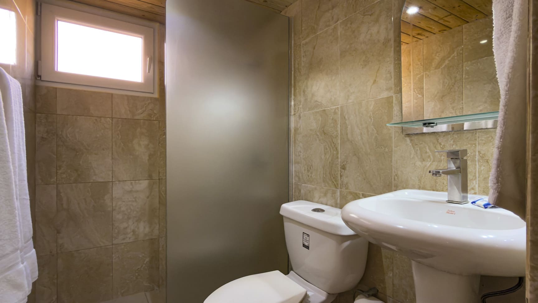 buyDRproperty Modern bathroom with a white toilet, sink, and frosted glass shower door. Sosua Real Estate