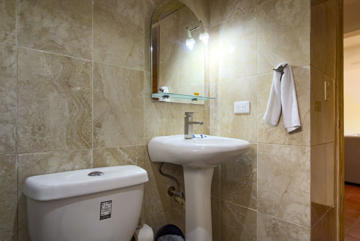 buyDRproperty Compact bathroom with white toilet, pedestal sink, and tiled walls. Sosua Real Estate