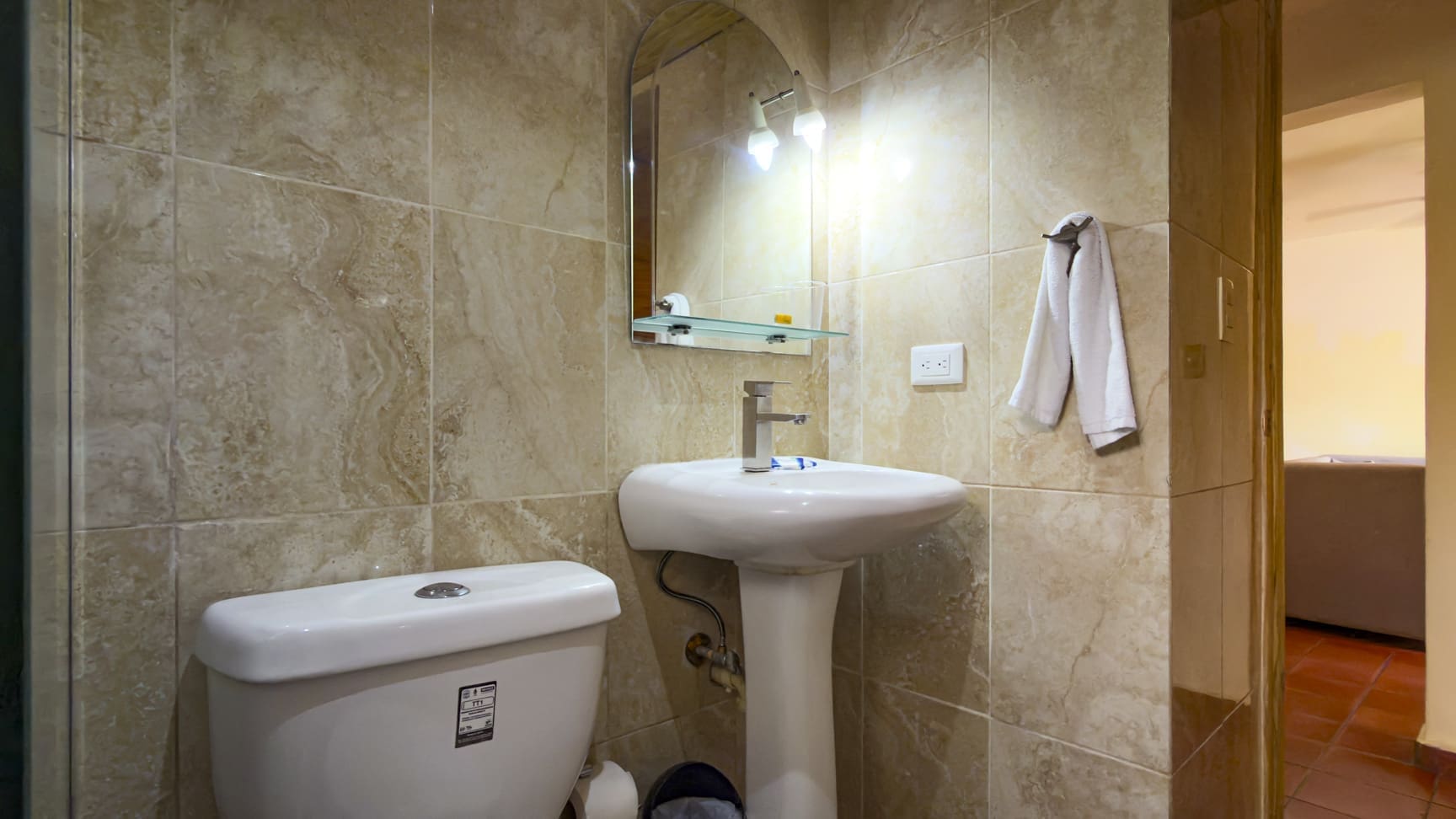 buyDRproperty Compact bathroom with white toilet, pedestal sink, and tiled walls. Sosua Real Estate