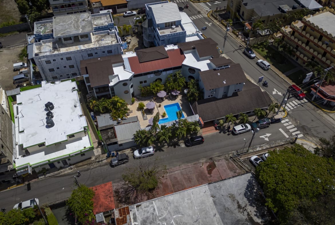 buyDRproperty Aerial view of a colorful Caribbean resort with a pool, surrounded by buildings and trees. Sosua Real Estate