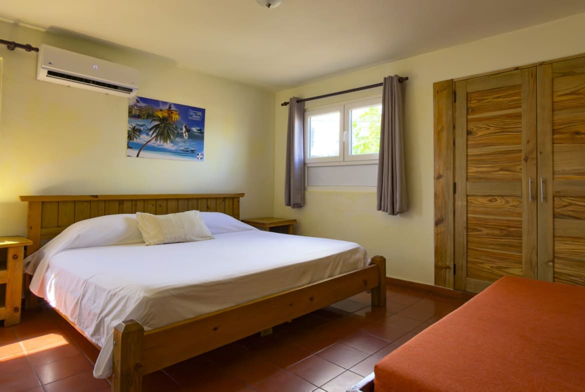 buyDRproperty Cozy bedroom with a king-size bed, wooden furniture, and tropical art. Sosua Real Estate