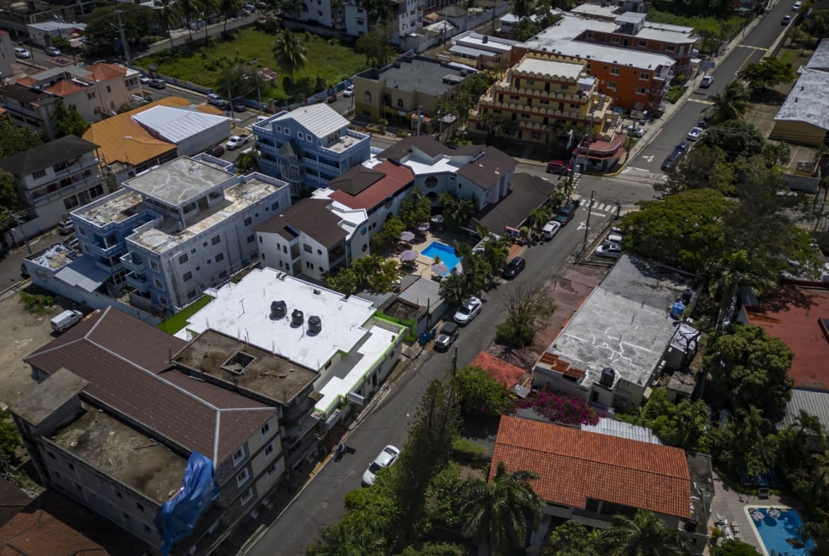 buyDRproperty Aerial view of a dense urban neighborhood with colorful buildings and palm trees. Sosua Real Estate