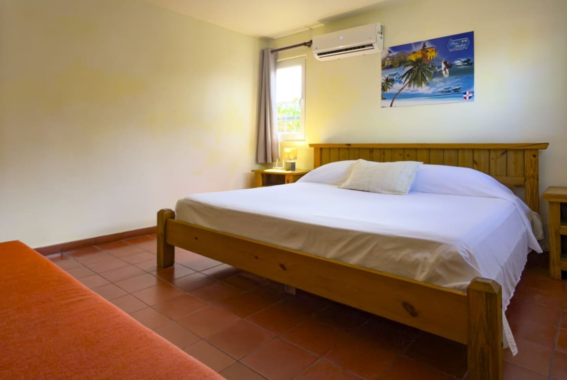 buyDRproperty Wooden bed with white sheets in a cozy bedroom with red tiles Sosua Real Estate