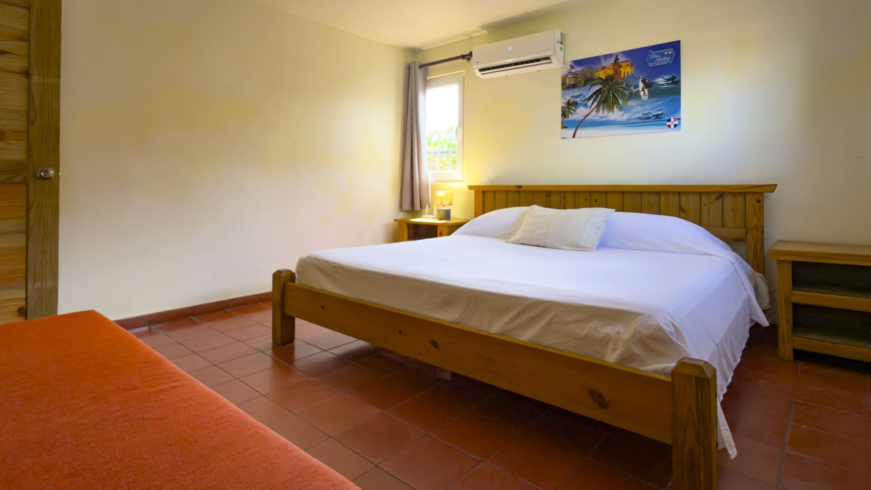 buyDRproperty Wooden bed with white sheets in a cozy bedroom with red tiles Sosua Real Estate