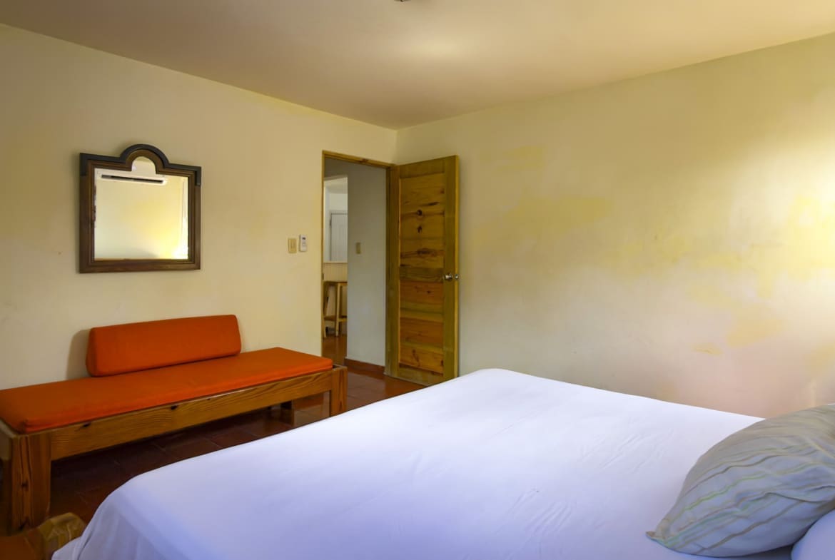 buyDRproperty Bright hotel bedroom with white bedding, orange bench, and wooden mirror Sosua Real Estate