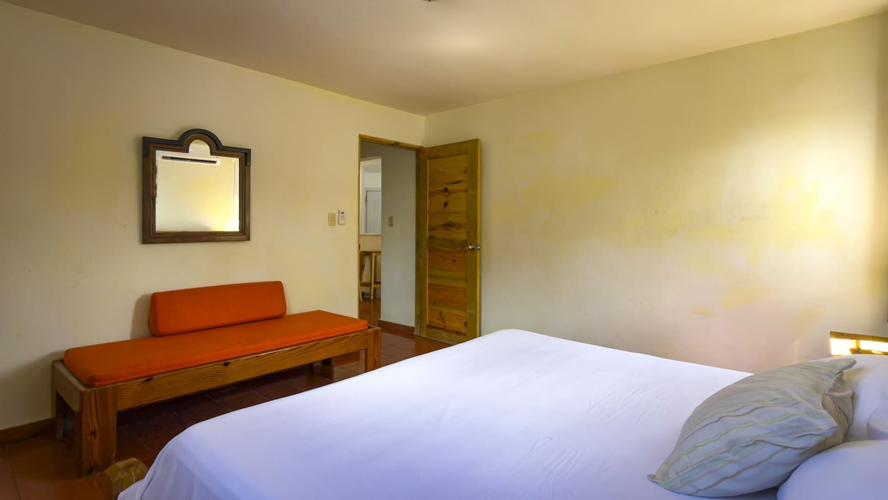 buyDRproperty Bright hotel bedroom with white bedding, orange bench, and wooden mirror Sosua Real Estate