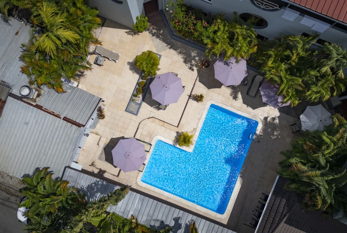 buyDRproperty Aerial view of a hotel courtyard with a bright blue swimming pool and purple umbrellas. Sosua Real Estate