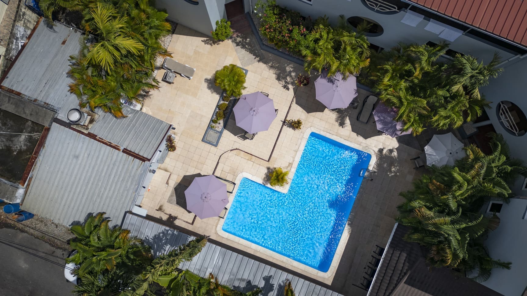 buyDRproperty Aerial view of a hotel courtyard with a bright blue swimming pool and purple umbrellas. Sosua Real Estate