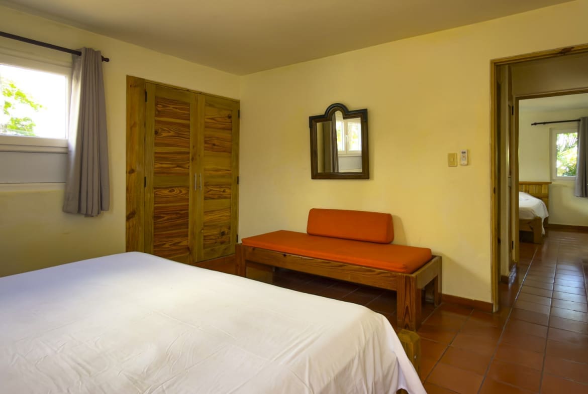 buyDRproperty Cozy bedroom with a white bed, orange bench, and wooden closet. Sosua Real Estate