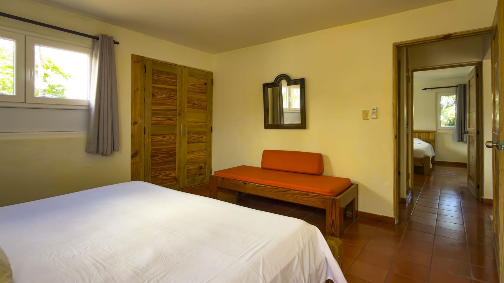 buyDRproperty Cozy bedroom with a white bed, orange bench, and wooden closet. Sosua Real Estate