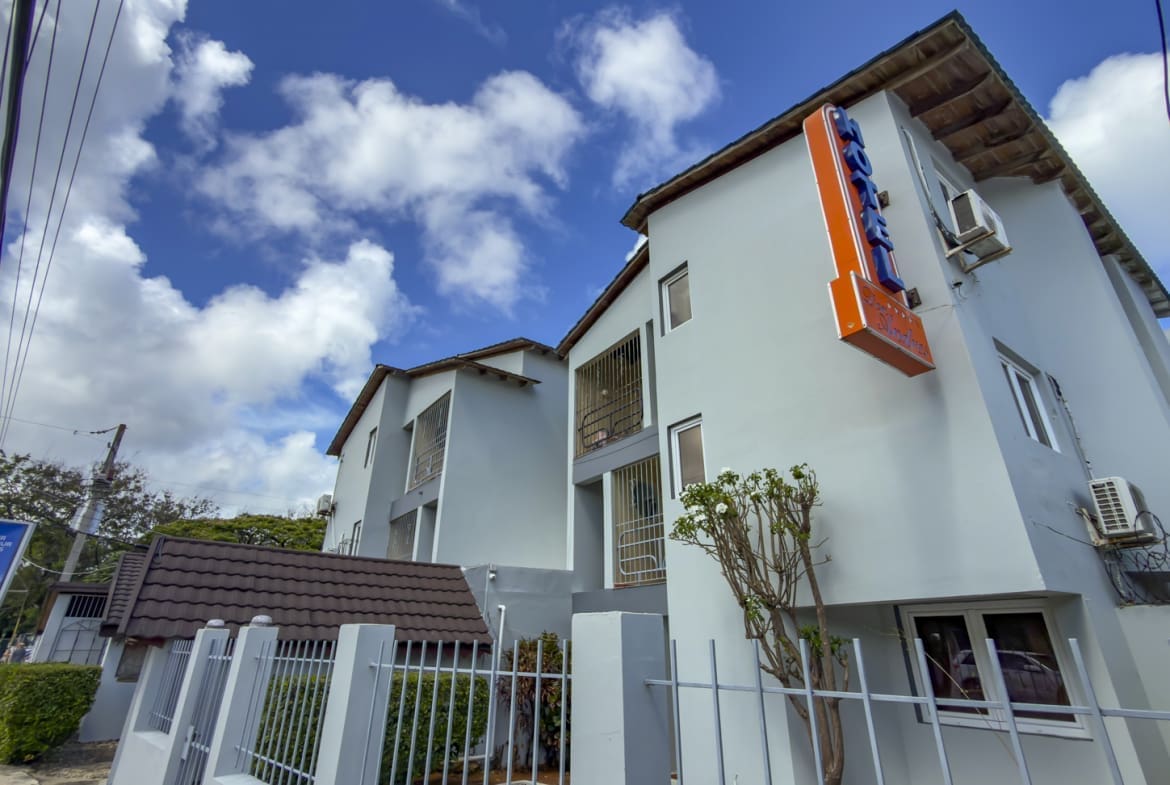 buyDRproperty Hotel building with bright blue sky and clouds, featuring a neon sign. Sosua Real Estate