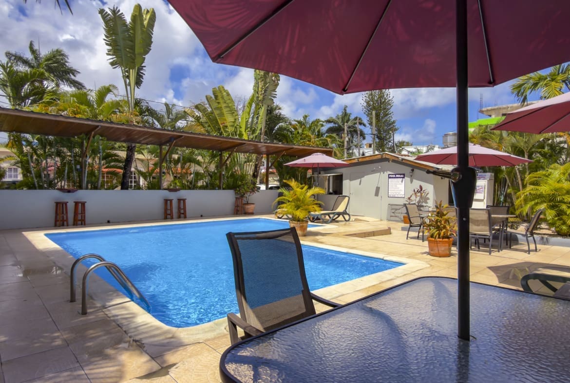 buyDRproperty Bright blue swimming pool with lounge chairs and umbrellas at a tropical resort. Sosua Real Estate