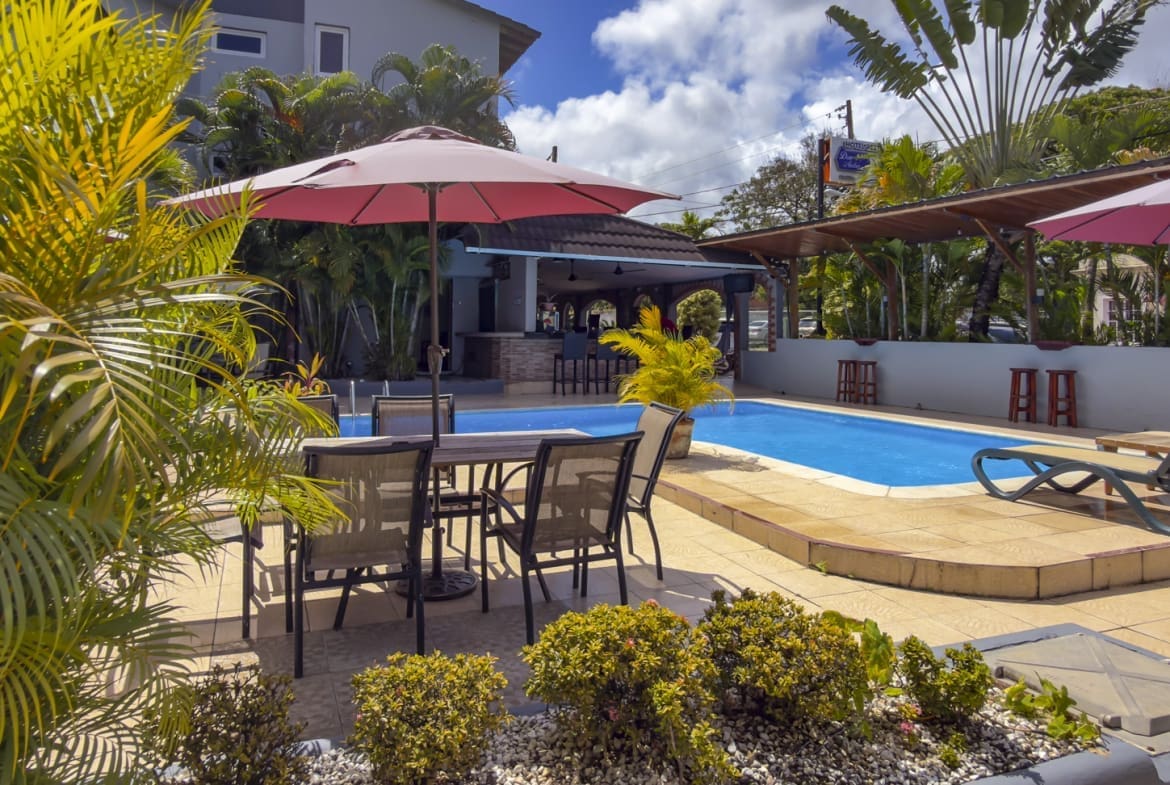 buyDRproperty Resort pool with lounge chairs, umbrellas, and tropical plants in sunshine. Sosua Real Estate
