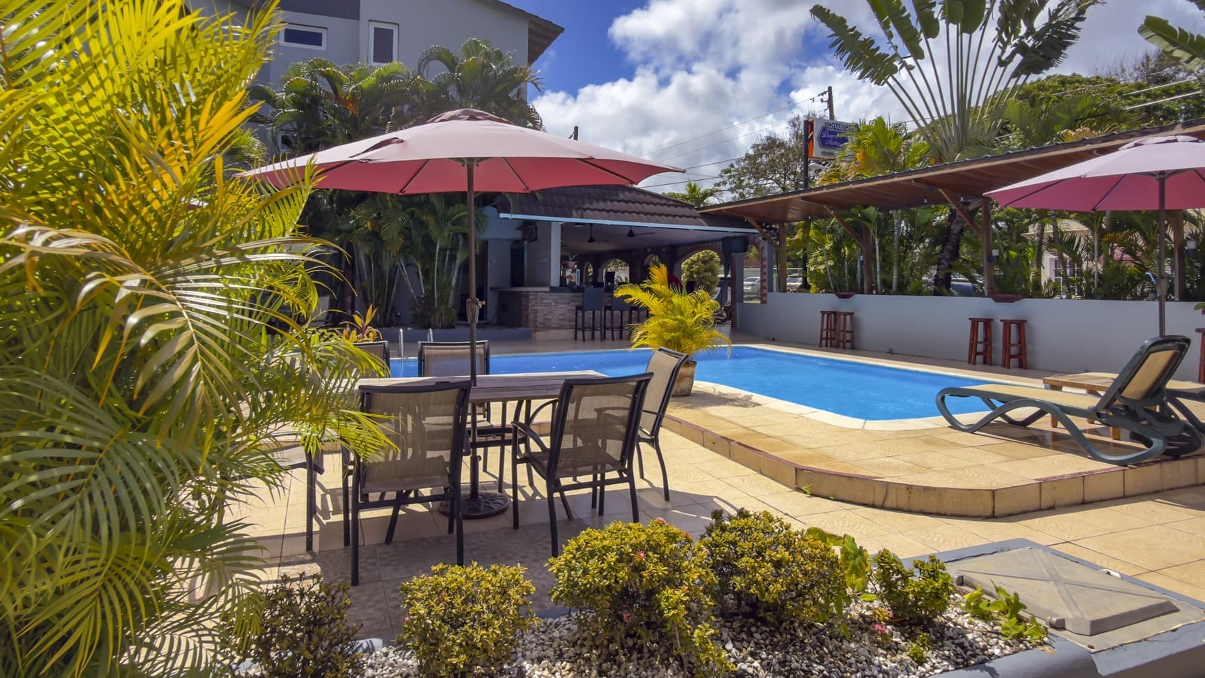 buyDRproperty Resort pool with lounge chairs, umbrellas, and tropical plants in sunshine. Sosua Real Estate