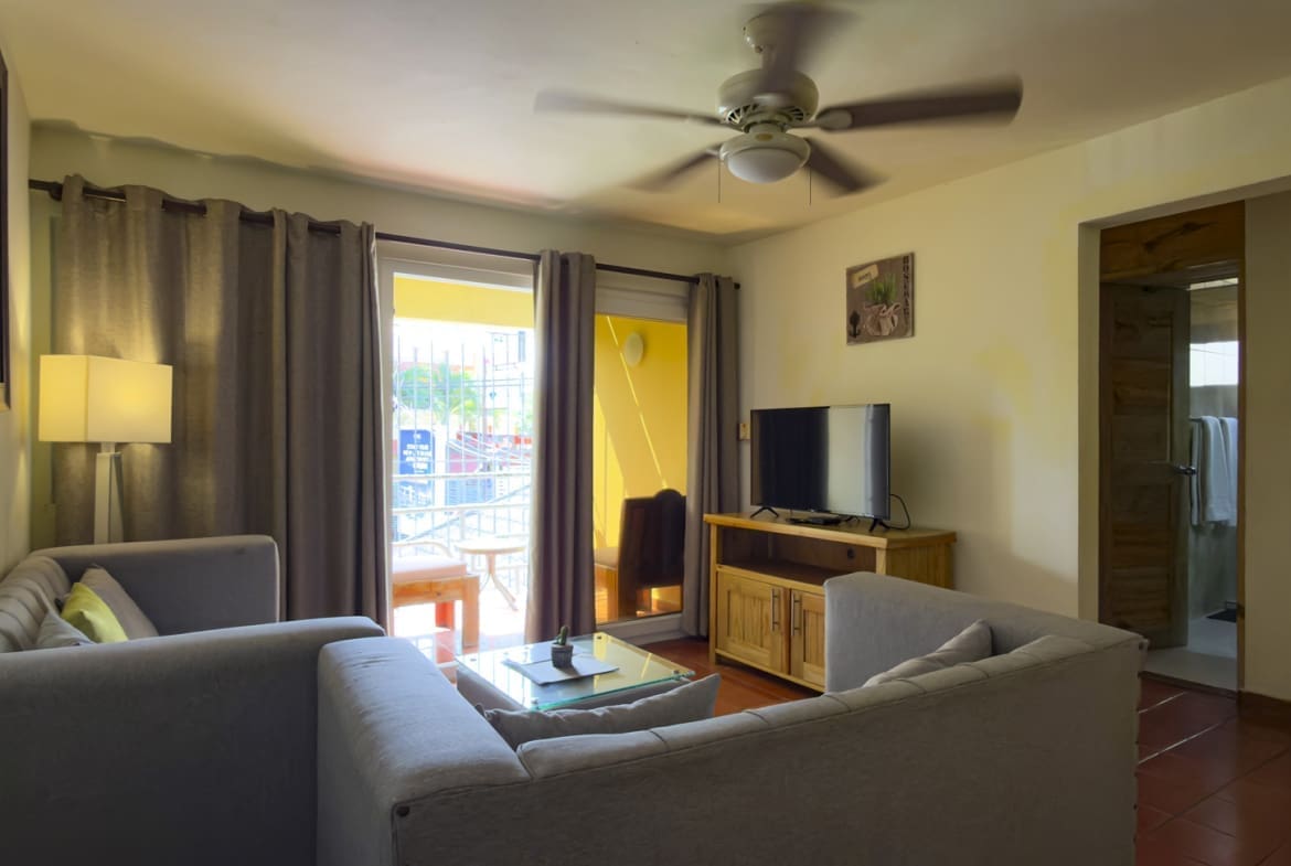 buyDRproperty Cozy living room with gray sectional sofa, glass coffee table, and TV. Sosua Real Estate