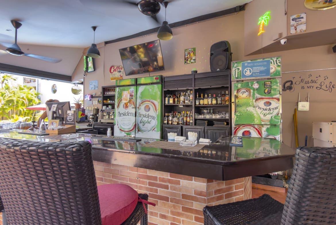 buyDRproperty Bar counter with refrigerators, bottles, and bar stools in a tropical setting. Sosua Real Estate