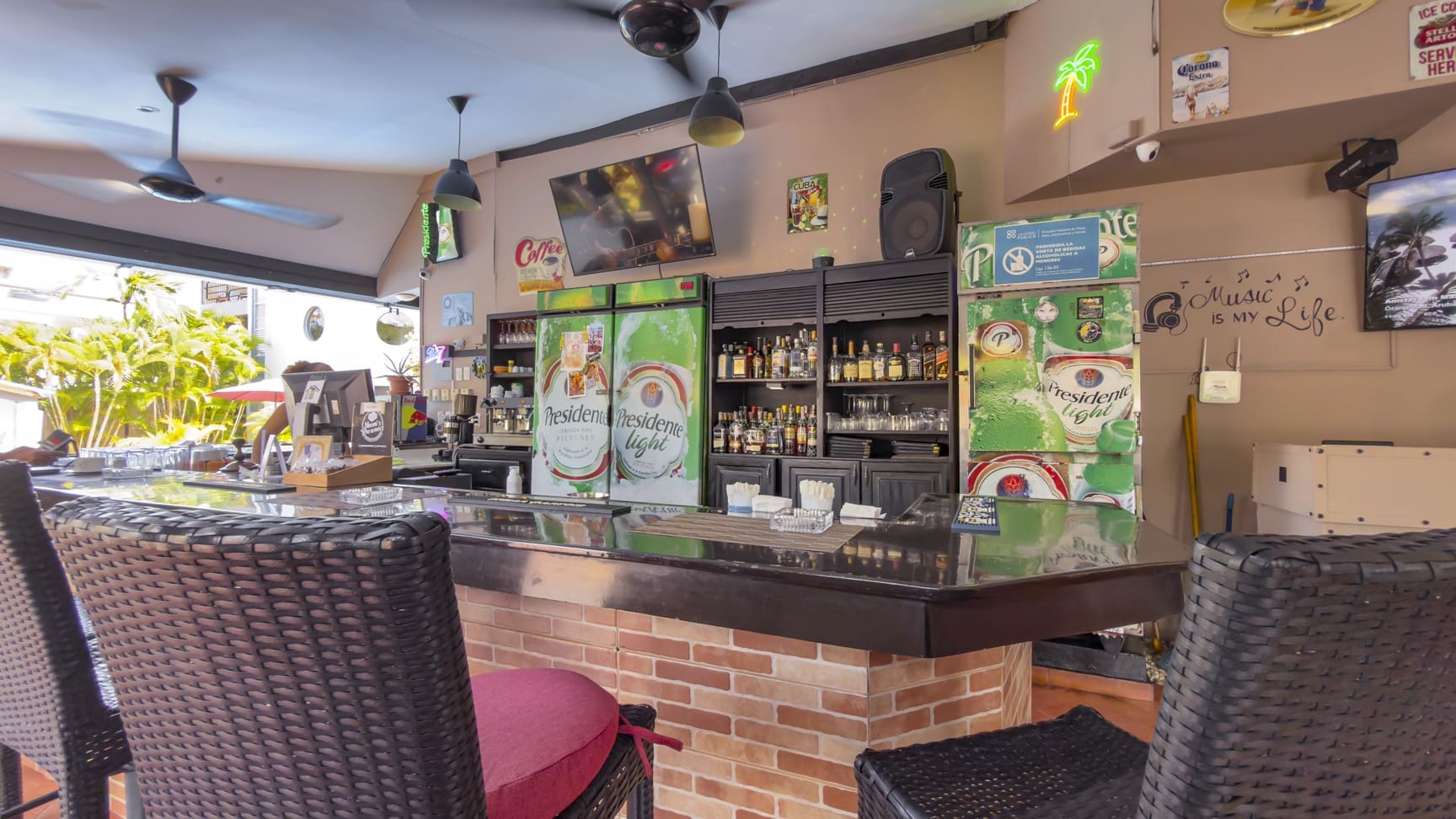buyDRproperty Bar counter with refrigerators, bottles, and bar stools in a tropical setting. Sosua Real Estate