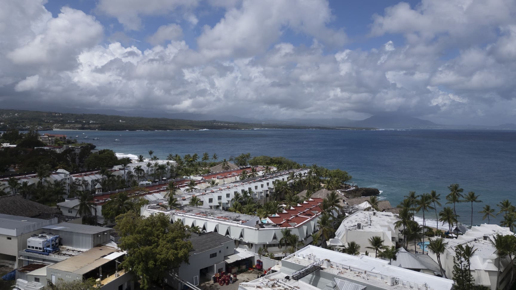 buyDRproperty Aerial view of a coastal resort with white buildings and palm trees overlooking the ocean. Sosua Real Estate