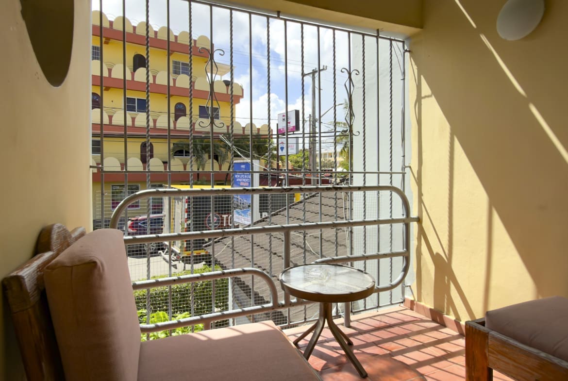 buyDRproperty Balcony with chair and table overlooking a colorful building in a tropical city. Sosua Real Estate