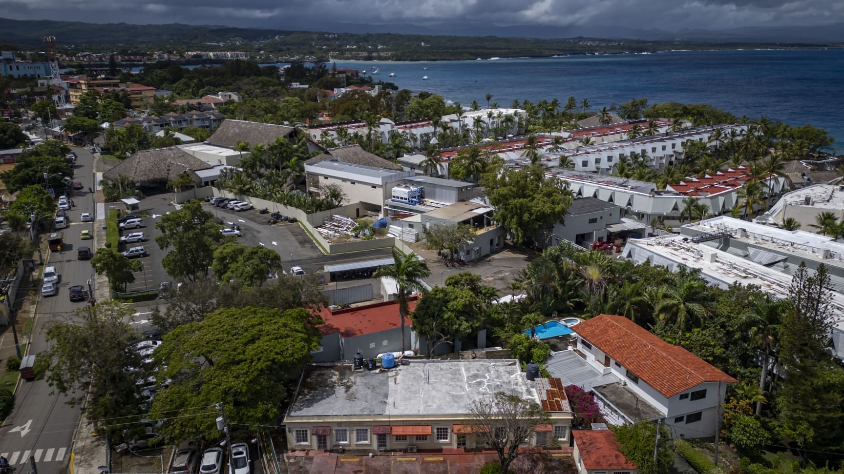 buyDRproperty Aerial view of a coastal town with buildings, roads, and the ocean under a cloudy sky. Sosua Real Estate