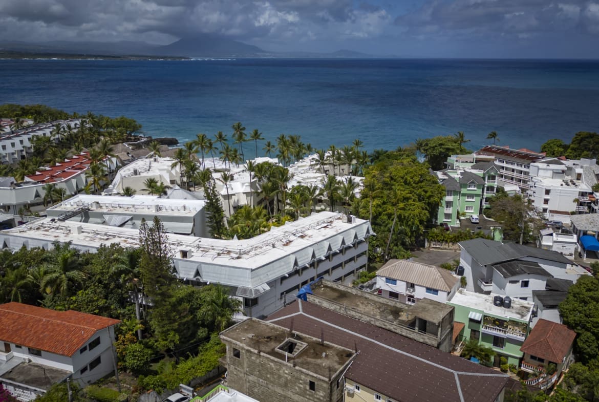 buyDRproperty Aerial view of coastal resort buildings and palm trees overlooking a blue ocean. Sosua Real Estate