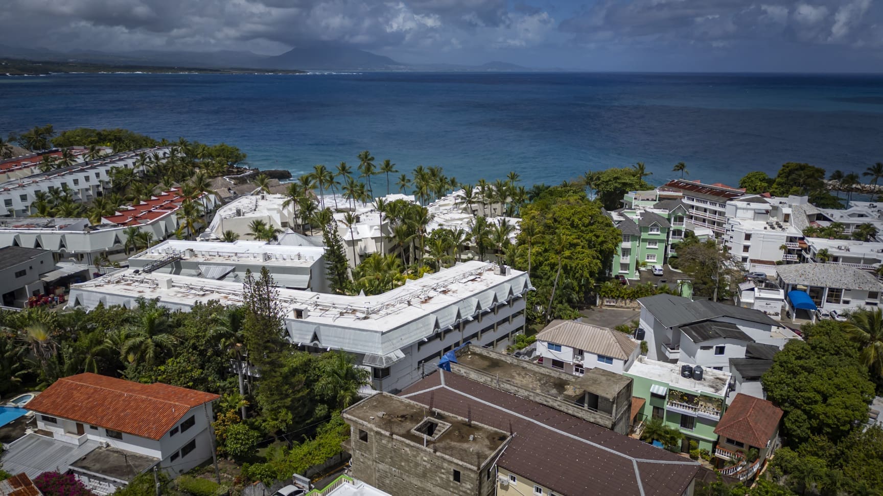 buyDRproperty Aerial view of coastal resort buildings and palm trees overlooking a blue ocean. Sosua Real Estate