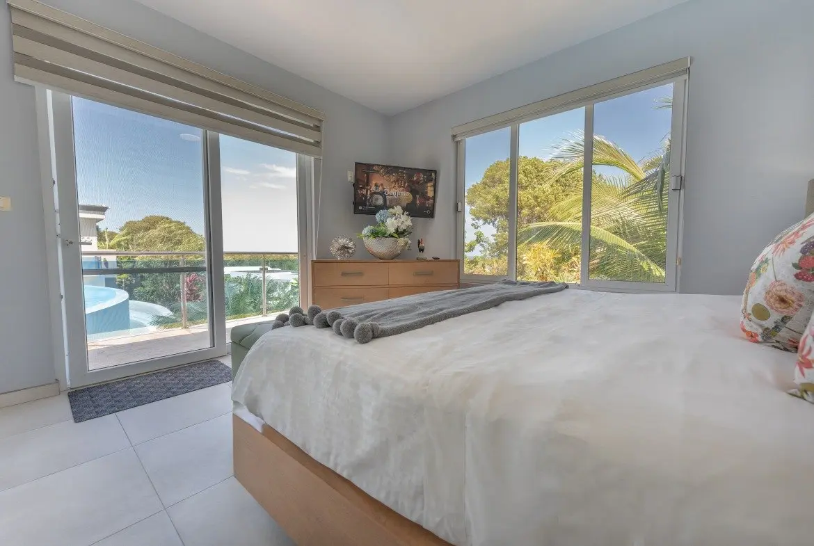 buyDRproperty Bedroom with large windows overlooking a pool and tropical foliage Sosua Real Estate
