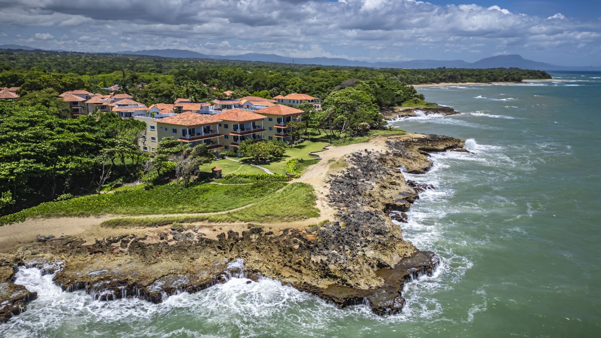 buyDRproperty Tropical resort with orange roofs nestled on a rocky coastline with turquoise ocean waves. Sosua Real Estate