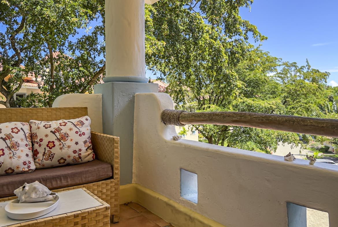 buyDRproperty Wicker sofa with owl pillows on a balcony with lush green trees and blue sky. Sosua Real Estate