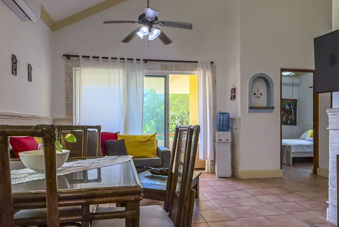 buyDRproperty Dining area with rattan chairs and table in a bright, open-plan living space with a sofa and sliding glass doors. Sosua Real Estate
