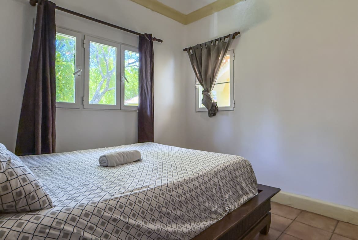 buyDRproperty Cozy bedroom with a bed, white walls, and a large window overlooking green trees. Sosua Real Estate