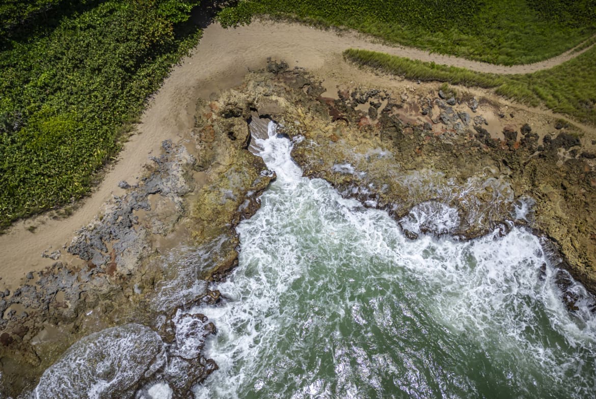 buyDRproperty Aerial view of a rocky coastline with crashing waves and lush green vegetation. Sosua Real Estate