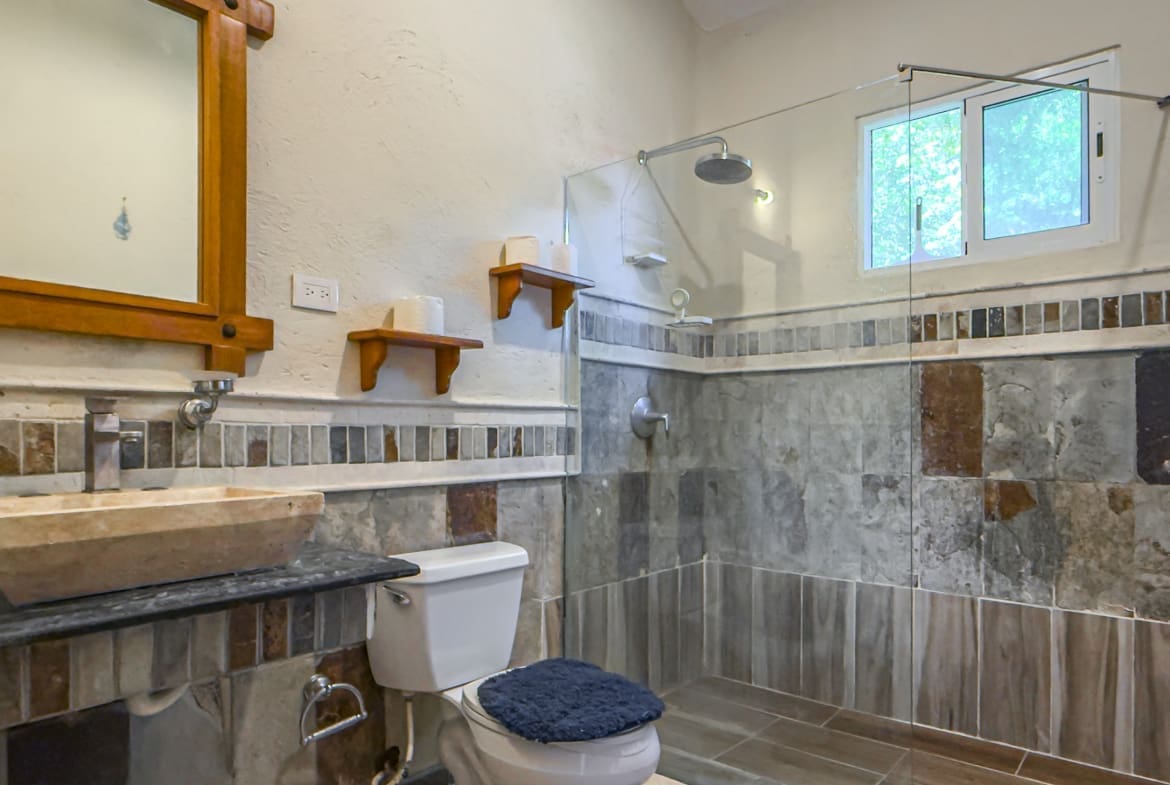 buyDRproperty Modern bathroom with stone sink, toilet, and walk-in shower with window. Sosua Real Estate
