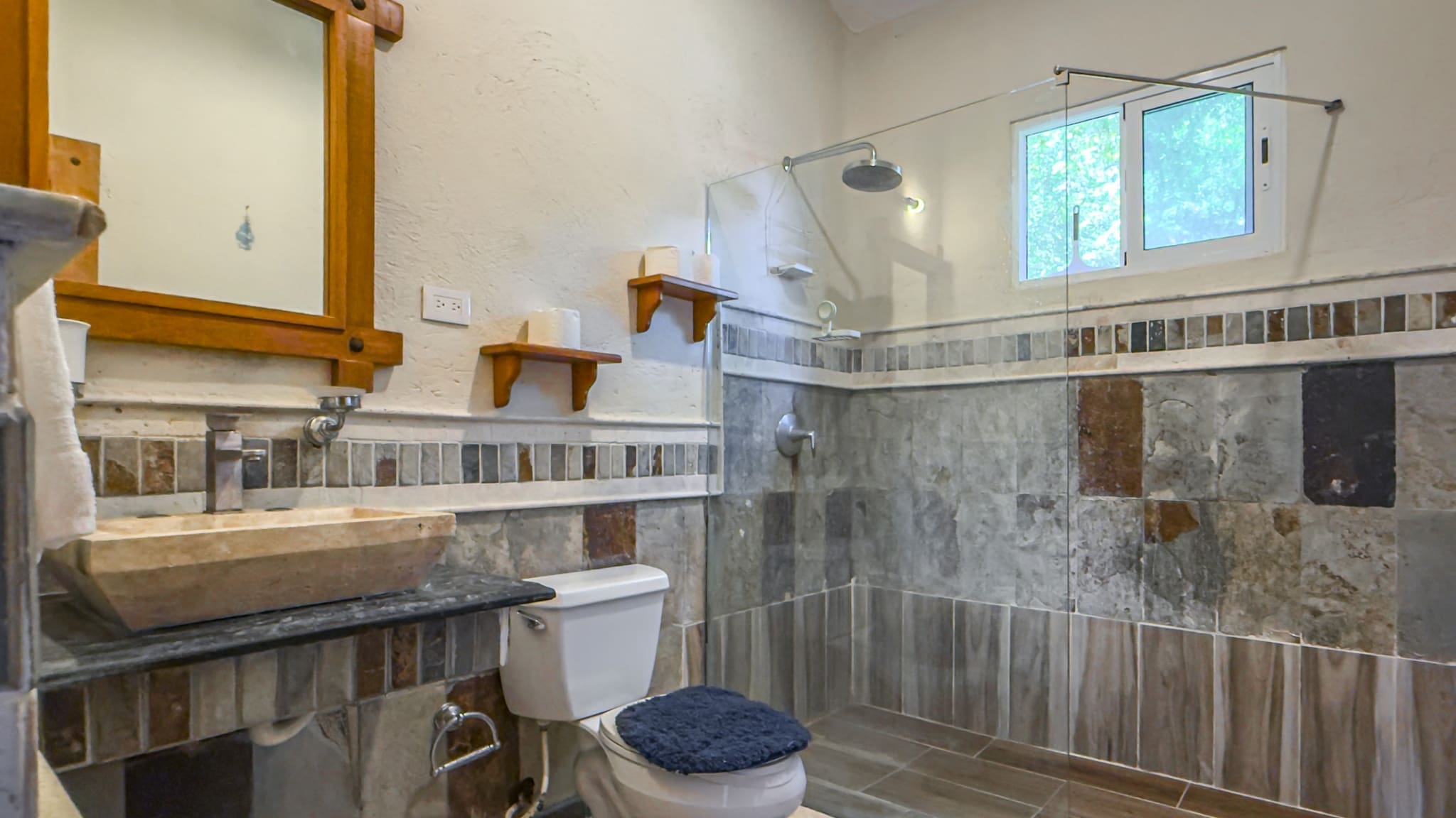 buyDRproperty Modern bathroom with stone sink, toilet, and walk-in shower with window. Sosua Real Estate