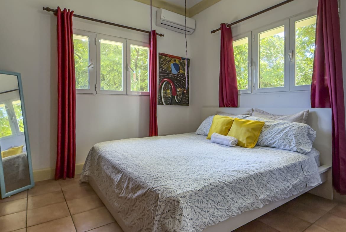 buyDRproperty Bright bedroom with a queen bed, yellow pillows, and red curtains Sosua Real Estate