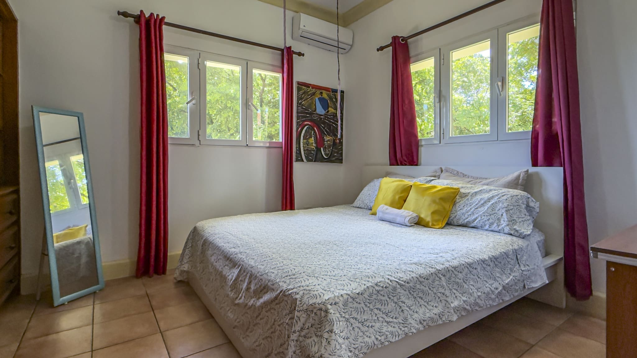 buyDRproperty Bright bedroom with a queen bed, yellow pillows, and red curtains Sosua Real Estate