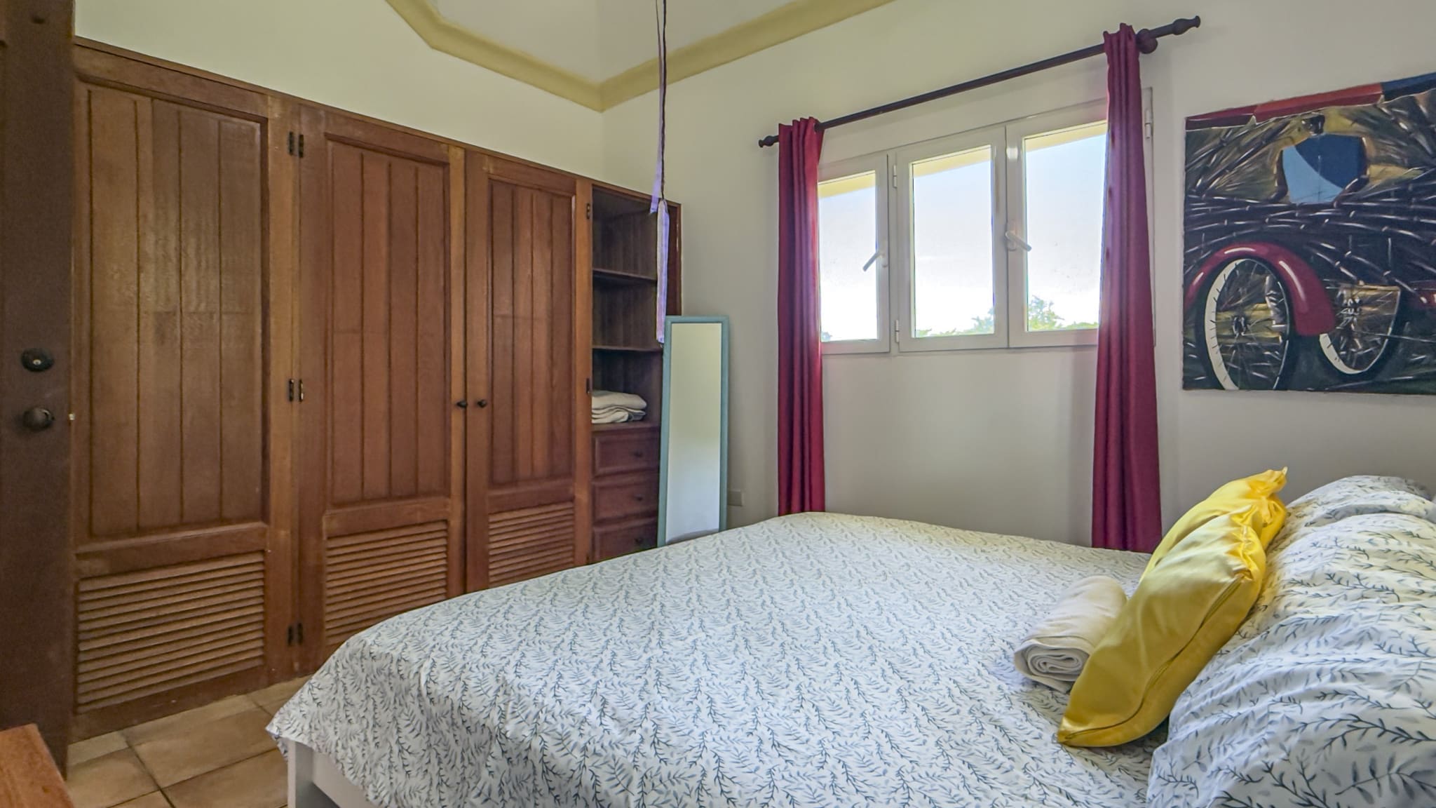buyDRproperty Bedroom with wooden wardrobes, bed with yellow pillows, and a window with red curtains. Sosua Real Estate